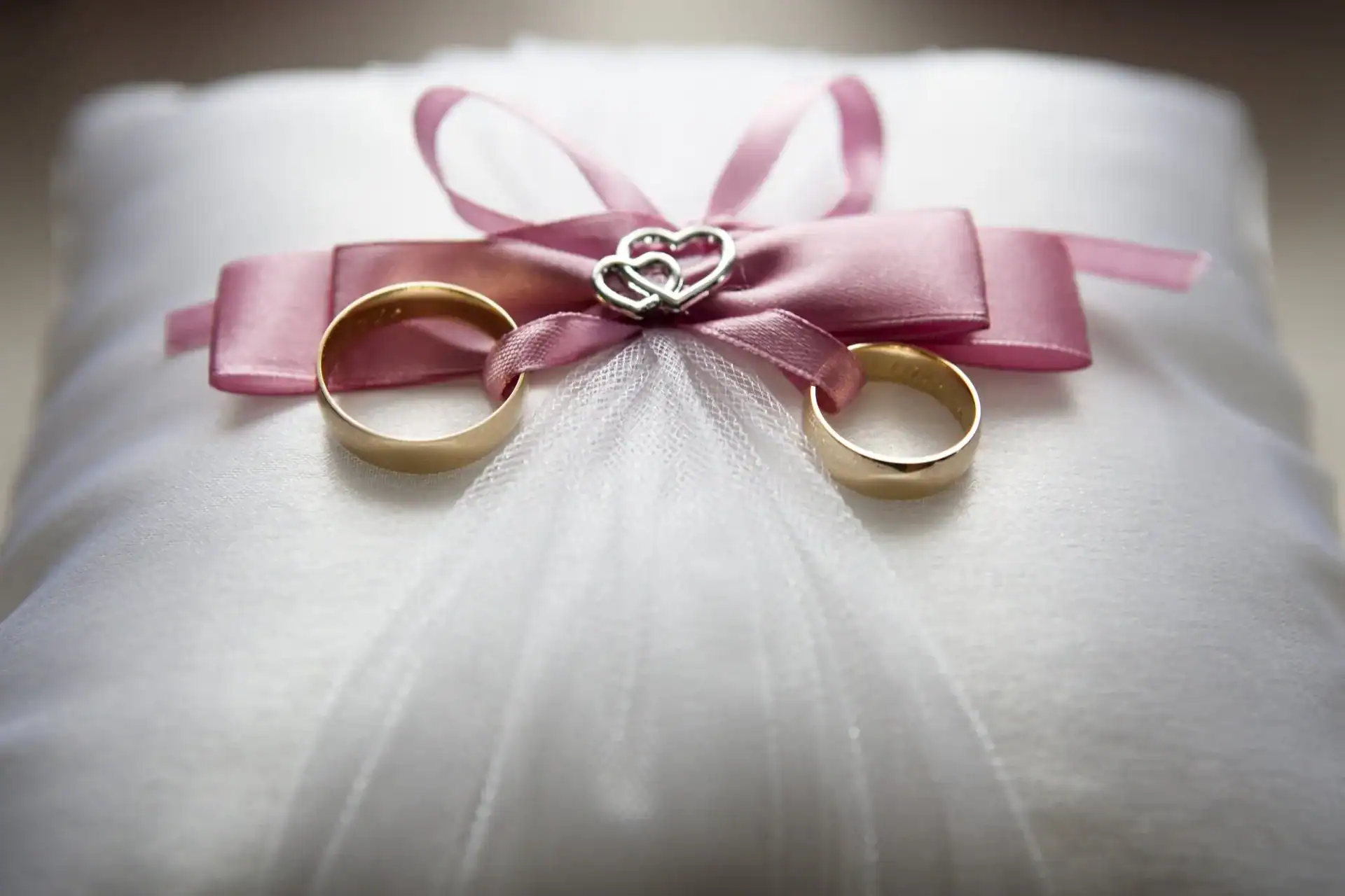 Wedding rings on satin pillow with pink ribbon, ideal for wedding ceremonies and vows.